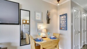 Un comedor con una mesa de madera, sillas y un espejo. Hay cuadros enmarcados en la pared y un cartel con texto.