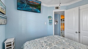 Une chambre à coucher avec un lit, un téléviseur fixé au mur et une porte donnant sur un placard.