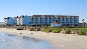 Un hotel frente a la playa con varios balcones, una playa de arena y cielo despejado.