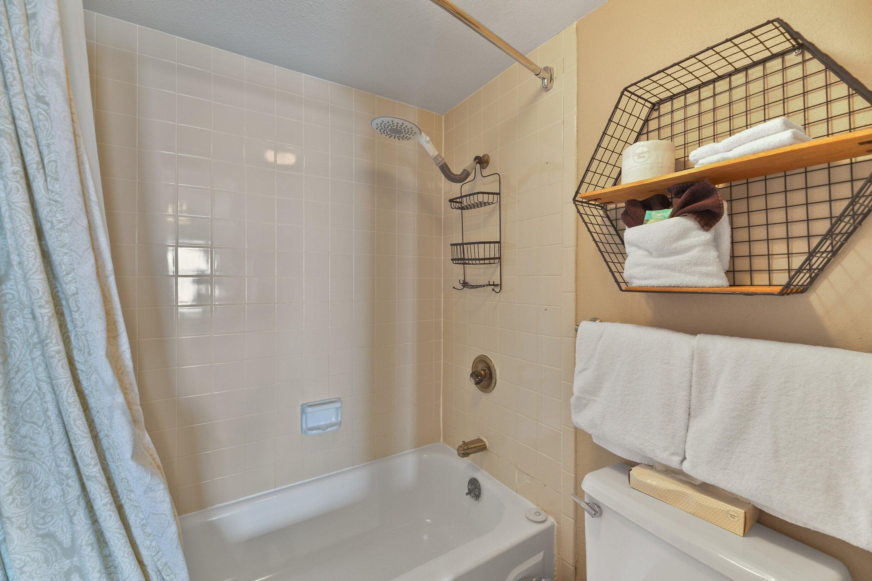 A bathroom with a bathtub, shower, and towel rack with towels.