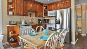 Una cocina con armarios de madera, un refrigerador de acero inoxidable, un microondas y una mesa de comedor con platos y vasos azules.