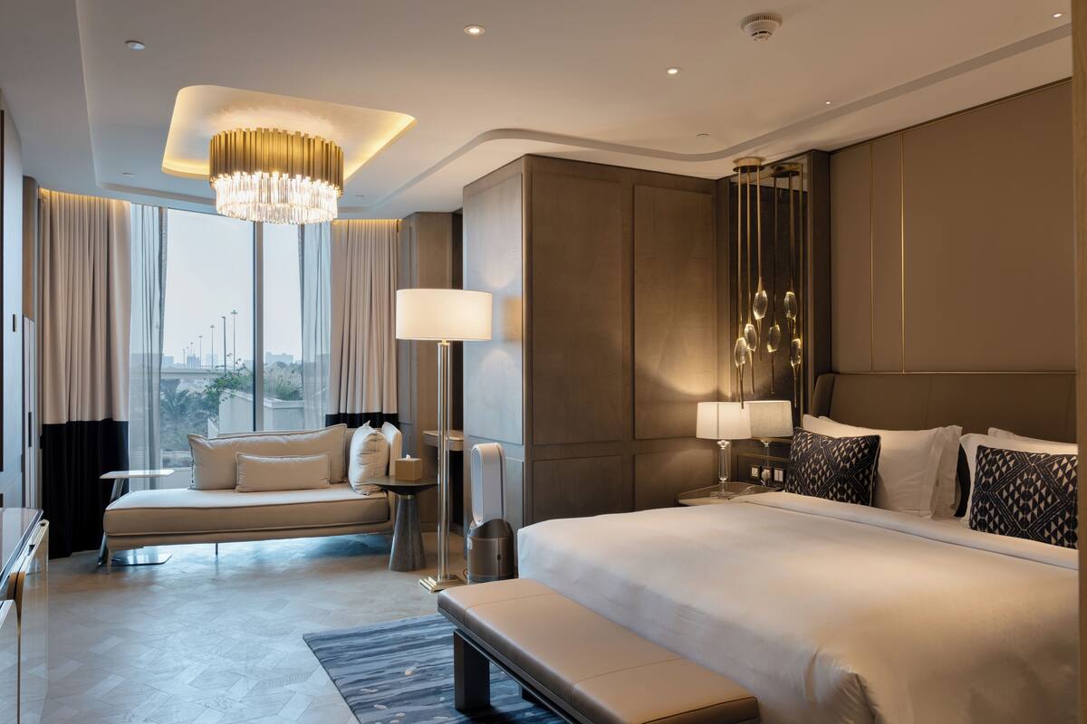 A modern hotel room with a large bed, a sofa, a bench, and a desk.