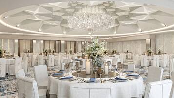 A banquet hall with round tables, white chairs, and a large chandelier.