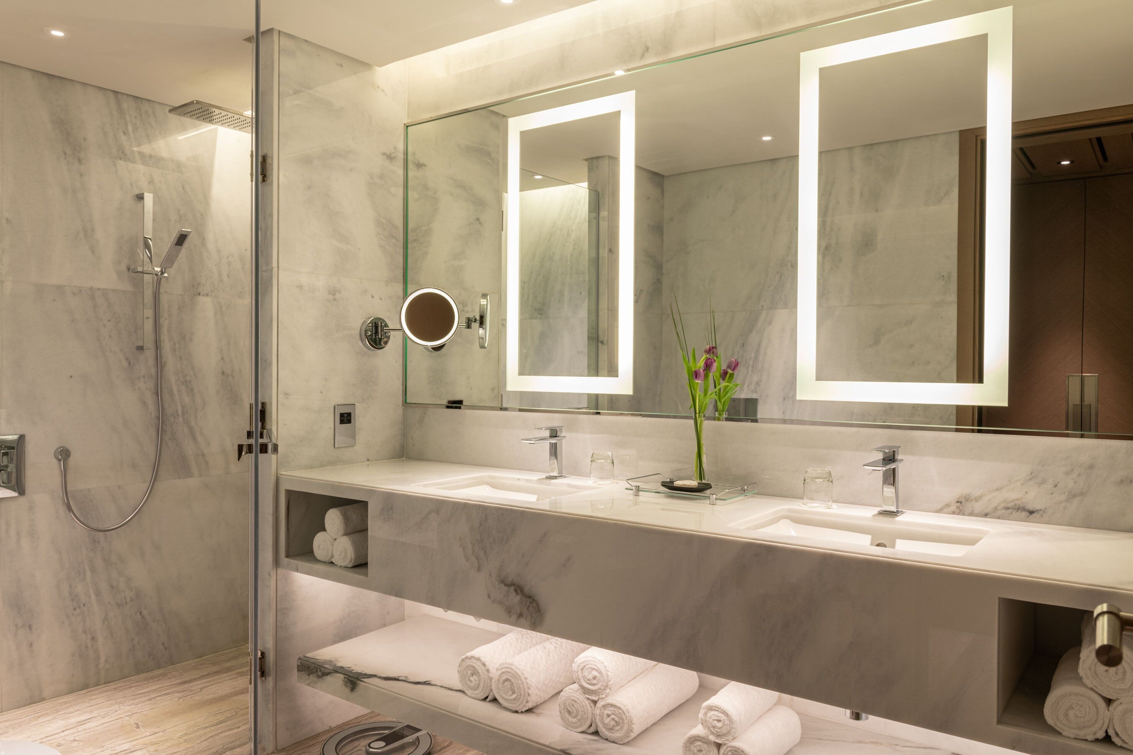 A modern bathroom with a glass-enclosed shower, two sinks, and a large mirror with integrated lighting.