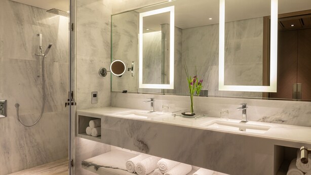 A modern bathroom with a glass-enclosed shower, two sinks, and a large mirror with integrated lighting.