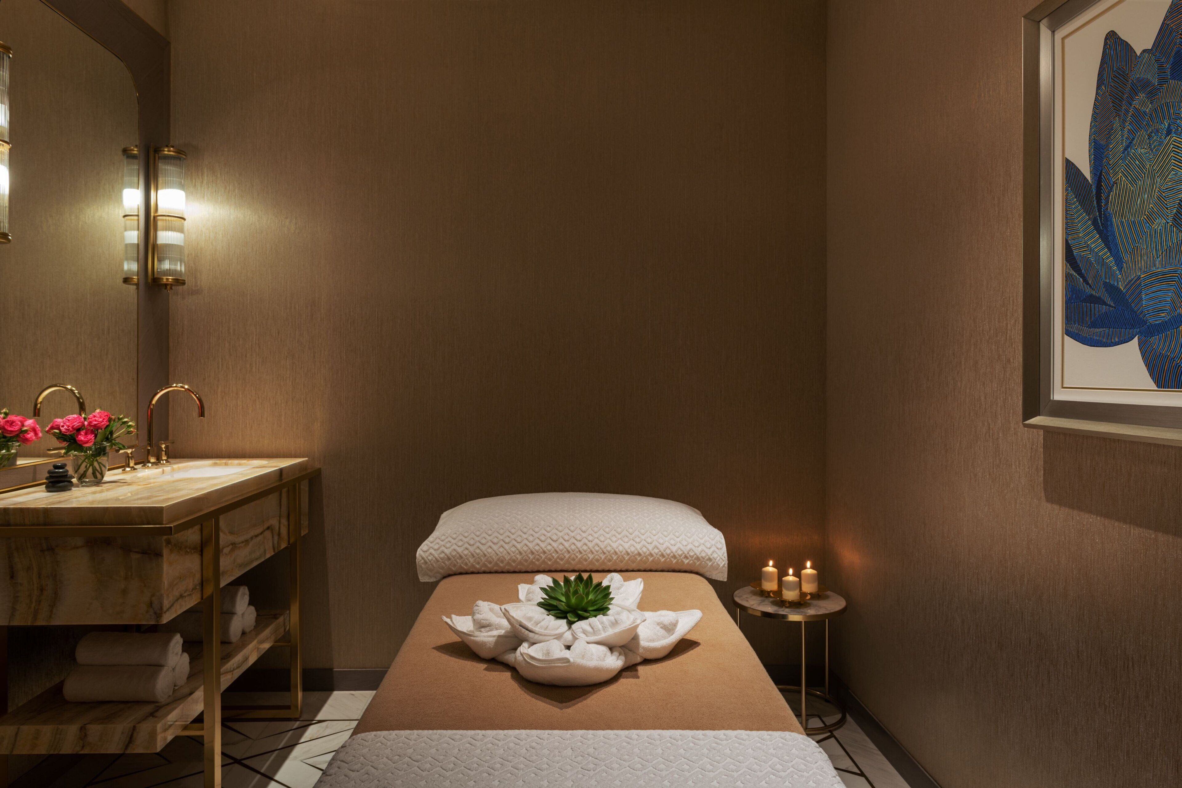A spa room with a wooden vanity, a massage table with towels and a green plant, and a wall-mounted artwork.