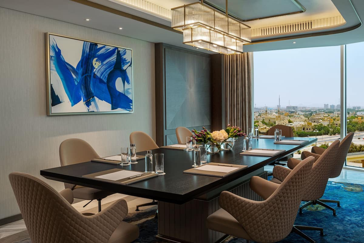 A modern conference room with a panoramic city view, a large abstract painting, and a chandelier.