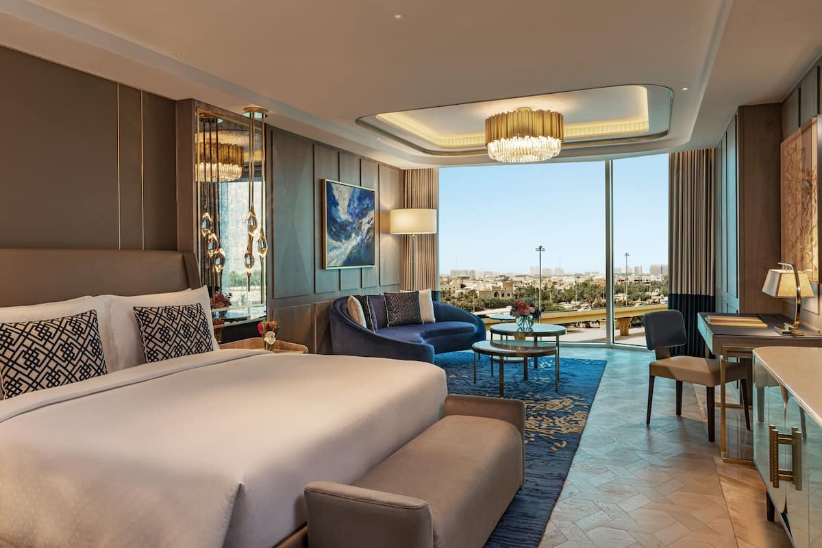 A modern hotel room with a large bed, a sofa, a desk, and a view of the city.