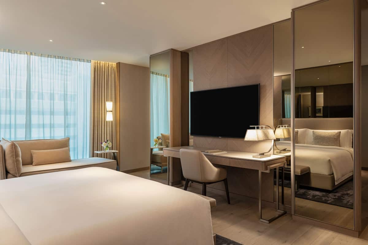 A modern hotel room with a large bed, a desk, a chair, a flat-screen TV, and a large mirror.