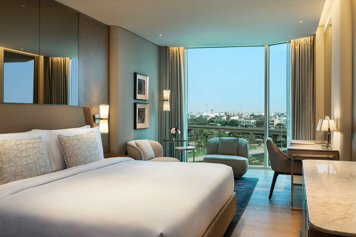 A hotel room with a large bed, a desk, a chair, and a view of the city.