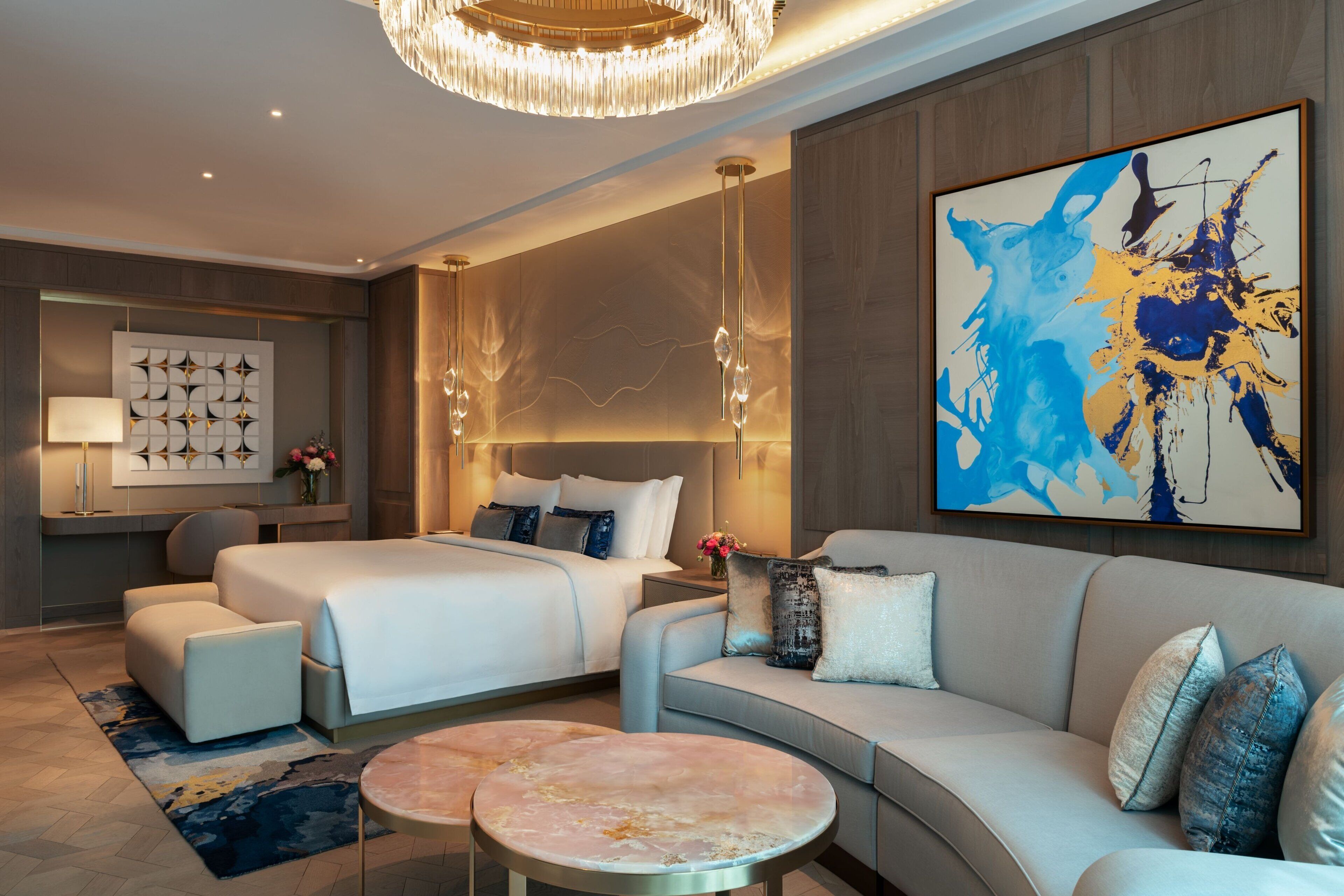 Una habitación de hotel moderna con una cama grande, un sofá, una mesa redonda y un cuadro abstracto de gran tamaño en la pared.
