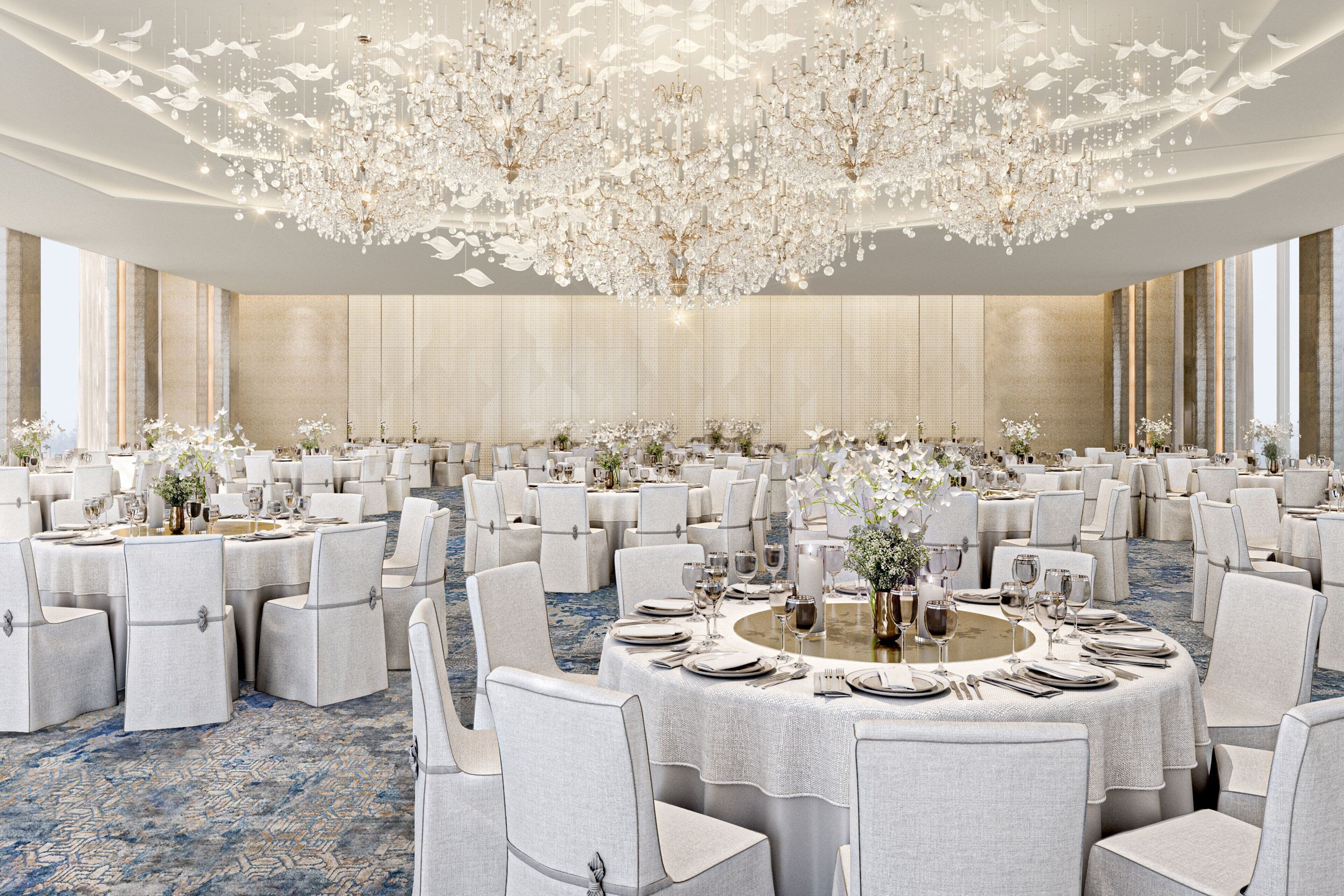A banquet hall with round tables, white chairs, and chandeliers.