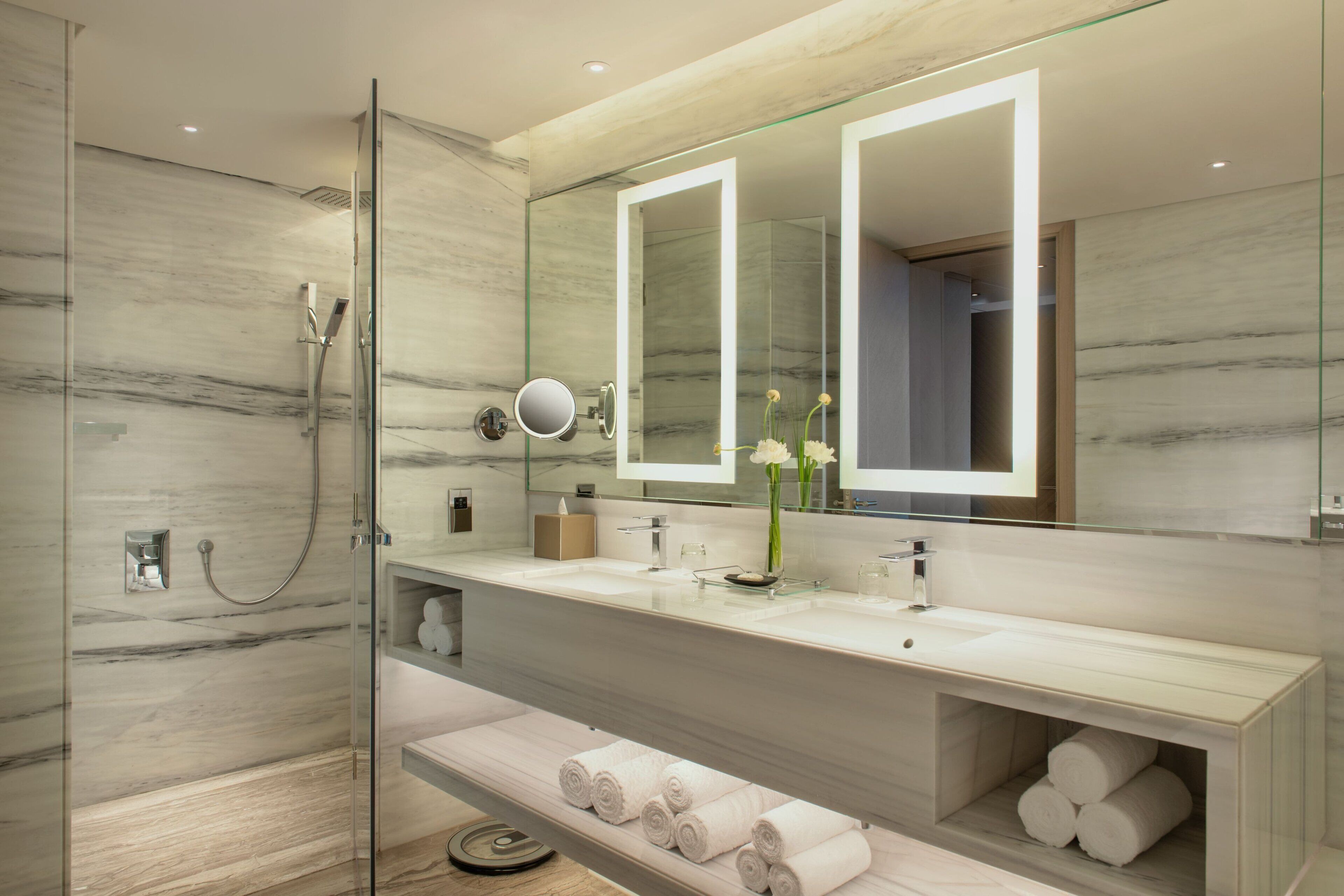 Un baño moderno con ducha envuelta en vidrio, un espejo grande y tocador con encimera de mármol.