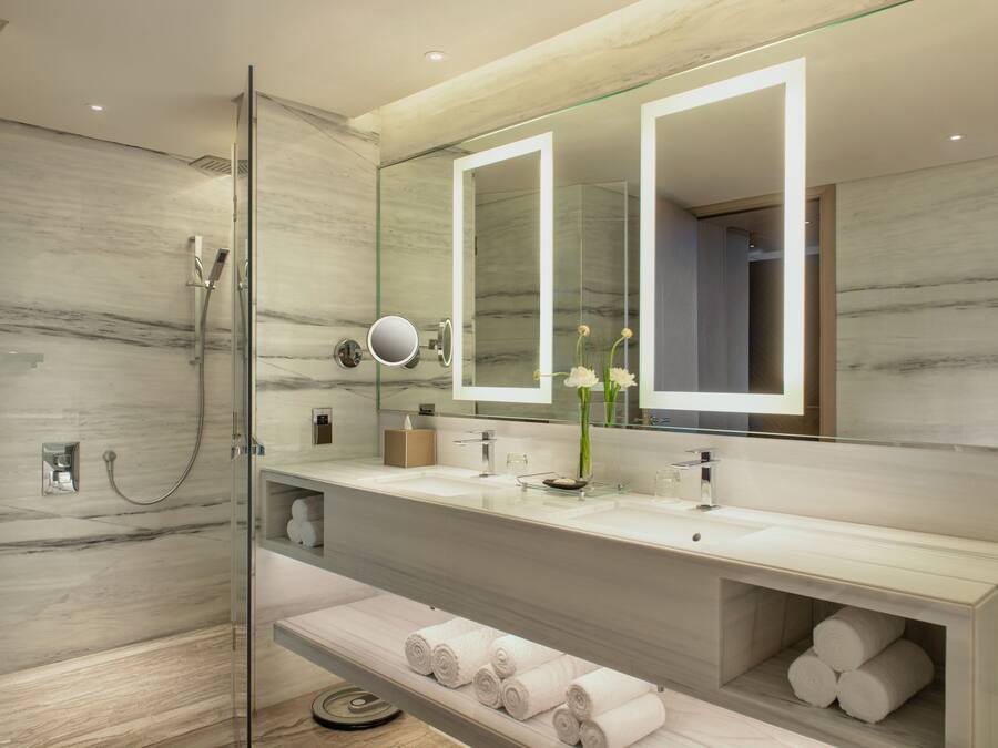 Un baño moderno con ducha envuelta en vidrio, un espejo grande y tocador con encimera de mármol.