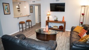 A modern living room with leather sofas, a glass coffee table, and a TV mounted on the wall. - Downtown Waterfront Condo (Pensacola)