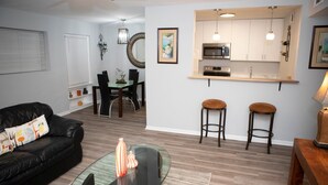 A modern living room with a black leather sofa, a glass coffee table, and a dining area with a wooden table and chairs. - Downtown Waterfront Condo (Pensacola)