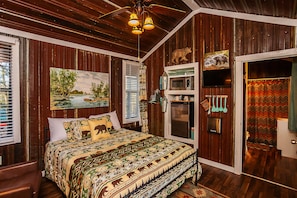 A bedroom with a bed, a painting, a television, a microwave, and a shower curtain. - Yeti Cabin (Benton)