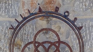 Un letrero de metal desgastado con un emblema circular y las letras 'V' y 'R' debajo, sujeto a una pared con textura.