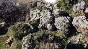 Un pueblo costero con edificios blancos, que incluye una iglesia con cúpula azul, rodeado de terreno rocoso y vegetación.