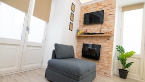 A modern living room with a grey sofa, a mounted TV, a stone wall, and a potted plant. - House La Dimora del Barbiere Catania (Catania)