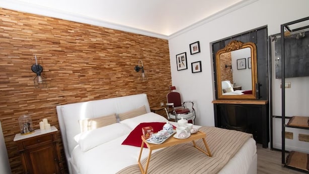 A modern bedroom with a wooden accent wall, a large bed, bedside tables, a tray with tea items, and a mirror. - House La Dimora del Barbiere Catania (Catania)