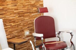 Ein roter Friseurstuhl mit Chrom-Armlehnen und einer weißen Fußstütze, vor einer Holzwand platziert.