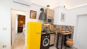 A compact kitchen with a washing machine, a microwave, a yellow refrigerator, and a small dining table with stools. - House La Dimora del Barbiere Catania (Catania)