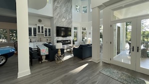 A spacious living area with a high ceiling, a fireplace, and a large TV. - Island Escape! Pool, Elevator, Pinball, Foosball, Arcade, Nursery,Infrared Sauna (Hilton Head Island)