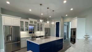 A modern kitchen with stainless steel appliances, a blue island, and pendant lighting. - Island Escape! Pool, Elevator, Pinball, Foosball, Arcade, Nursery,Infrared Sauna (Hilton Head Island)