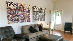 Ein Wohnzimmer mit Ledersessel, Sofa und Hocker. An der Wand befinden sich zwei große abstrakte Gemälde.