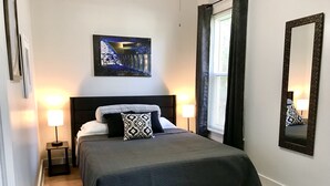 Ein ordentlich eingerichtetes Schlafzimmer mit einem Bett, zwei Nachttischlampen, einem großen Spiegel und einem Bild an der Wand.