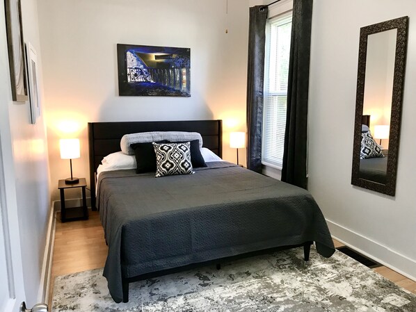 Une chambre à coucher bien rangée, avec un lit, deux lampes de chevet, un grand miroir et un tableau accroché au mur.