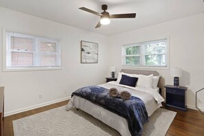 A bedroom with a bed, two nightstands, a ceiling fan, and two windows with blinds.