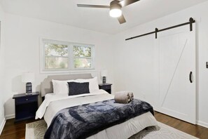Un dormitorio con cama, mesita de noche, lámpara de noche, ventana con persianas, ventilador de techo y puerta corredera.