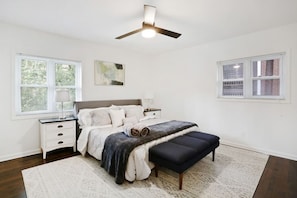 Quarto com cama, mesas de cabeceira, ventoinha no teto e janelas.