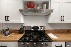 A modern kitchen with white cabinets, a stainless steel range hood, a gas stove, and a wooden countertop.