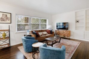 Una sala de estar con un sofá, dos sillones, una mesa de centro, un televisor y una estantería.