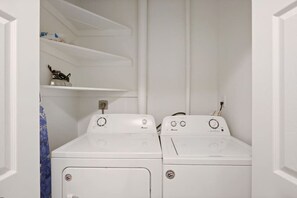 Une buanderie équipée de deux machines à laver à chargement frontal, toutes deux de couleur blanche, et d’une étagère placée au-dessus.