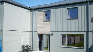 A two-story building with a flat roof, a sliding glass door entrance, and a small patio area with outdoor furniture. - Alpine View - a cosy Aviemore family home (Aviemore)