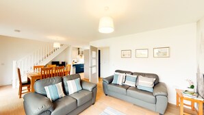 A modern living room with two grey sofas, a wooden dining table, and a staircase leading to the upper floor. - Alpine View - a cosy Aviemore family home (Aviemore)