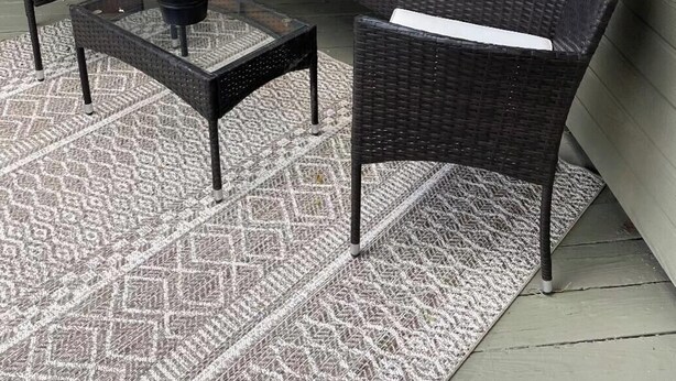 Ein Patio mit Korbmöbeln, darunter zwei Stühle und ein Tisch, sowie einem gemusterten Teppich.
