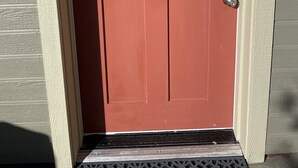 Eine rote Tür mit einem weißen Fensterrahmen und einem Klingelknopf aus Metall.