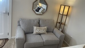 Ein Wohnzimmer mit grauem Sofa, einem Zierkissen, einem Spiegel und einer Stehlampe.