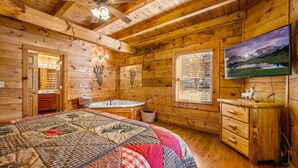 Ein Schlafzimmer einer Holzhütte mit einem großen Bett, einer Badewanne, einem Fernseher und Blick auf die Berge.