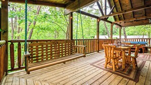 Eine Holzterrasse mit einer Bank und einem Tisch, umgeben von einem Holzgeländer, mit Blick auf eine bewaldete Landschaft.
