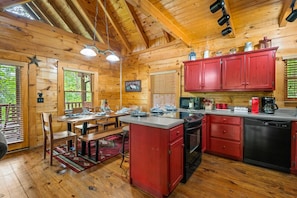 L’intérieur d’un chalet en bois comprend un espace cuisine avec des meubles de rangement rouges, une table à manger et un coin café.