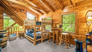 Ein gemütliches Blockhauszimmer mit Etagenbetten, einem kleinen Tisch und einem Fenster mit Blick auf Grünflächen.
