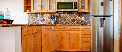 A kitchen with wooden cabinets, a stainless steel refrigerator, a microwave, and granite countertops.
