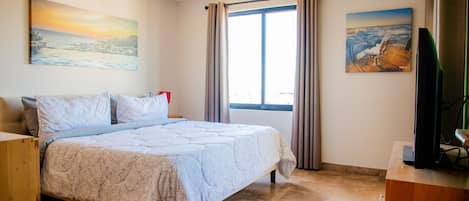 A bedroom with a bed, a ceiling fan, a window with curtains, and artwork on the walls.