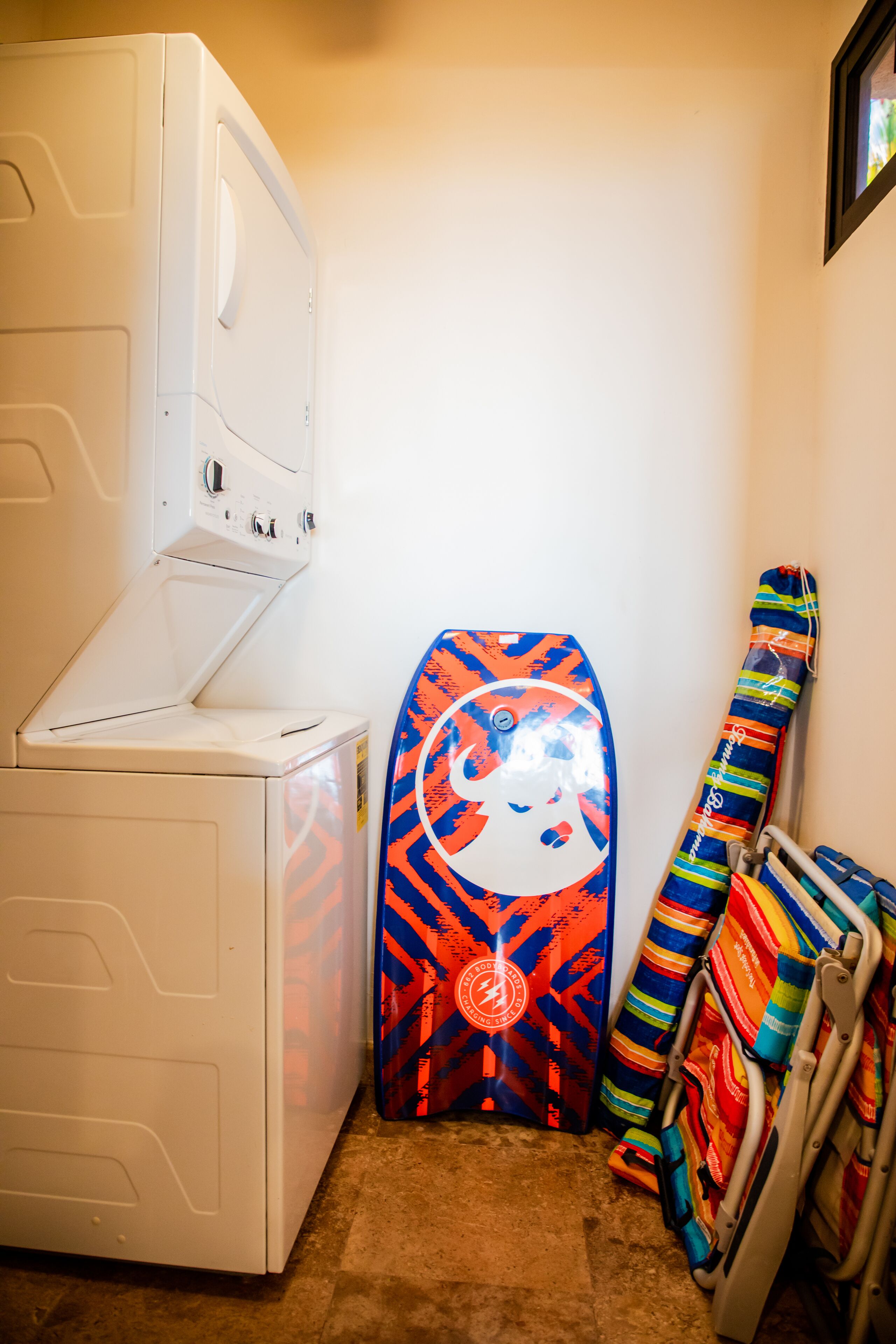 Un espace buanderie comprenant un lave-linge, une planche de surf aux couleurs vives et un porte-serviettes avec des serviettes pliées.